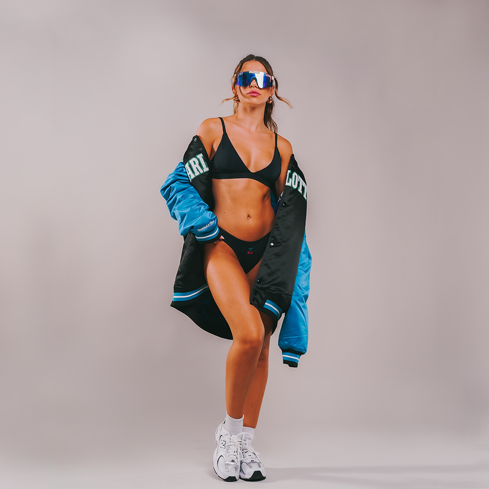 cheeky cherry ultra smooth leakproof dipped thong and bralette styled on model with an oversized coach's jacket, sunglasses and sneakers. button for influencers to contact us and collab